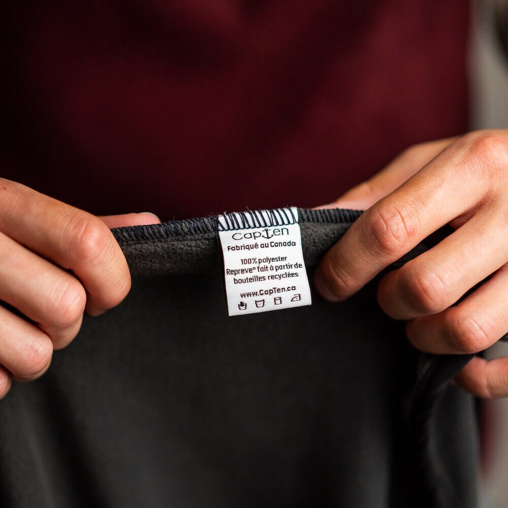 Person holding a fleece with a focus on the label which has Made in Canada written on it